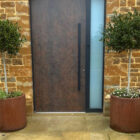 A fully weathered pair of CorTen steel cylindrical planters by Weather It, set as entranceway markers and planted with olive trees