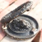 An antique cast iron door knocker with lion head and garland design, showing peeling paint and mild corrosion.