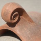 Detail of the scrollwork on a reclaimed decorative finial ridge tile showing the light weathering and rich colour
