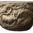 A reclaimed composite stone Norman style planter showing weathering and an animal theme.