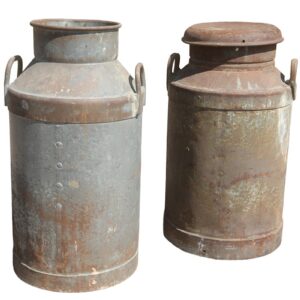 A pair of reclaimed steel milk churns showing weathered surfaces and an aged patina alongside the original dairy's name.