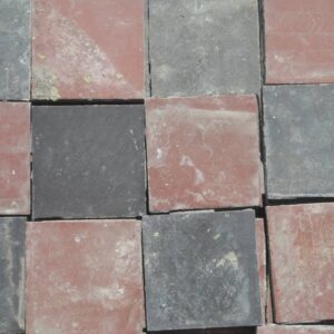 Reclaimed red and black quarry tiles in a classic chequerboard pattern and showing the remnants of mortar and dust from the process of reclamation.