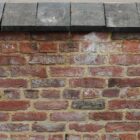 A run of blue square edge saddleback wall copings showing the delightful contrast against a wall of reclaimed red bricks.