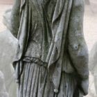 A statue of a woman holding a jug showing the fine detail in the folds of clothing and with a fine patina
