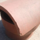 Detail of a terracotta cowled chimney pot or flue cap showing minor chips on the edges from years in storage.