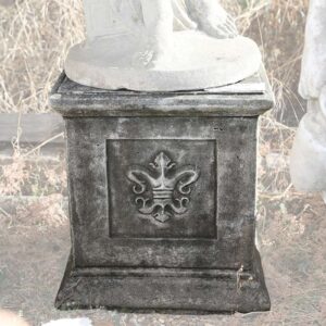 A weathered composite stone plinth witha stylised fleur de lis crest as decorative motif