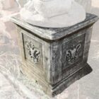 A weathered composite stone plinth witha stylised fleur de lis crest as decorative motif