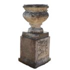 A weathered composite stone urn on pedestal, with an aged patina and standing 37 inches high