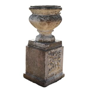 A weathered composite stone urn on pedestal, with an aged patina and standing 37 inches high
