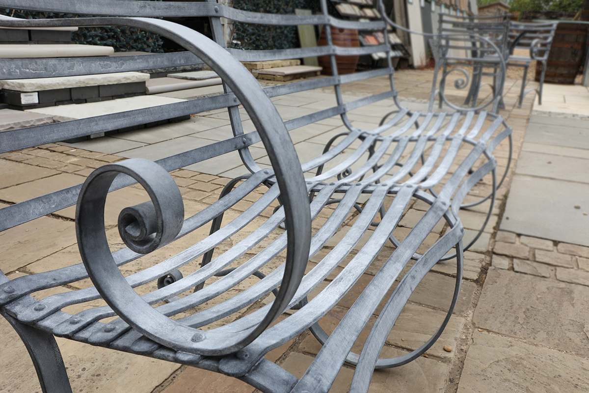 Detail of the impressive four seater zinc plated garden bench from The Suffolk Collection, showing the hand etched finish and elegant scrollwork