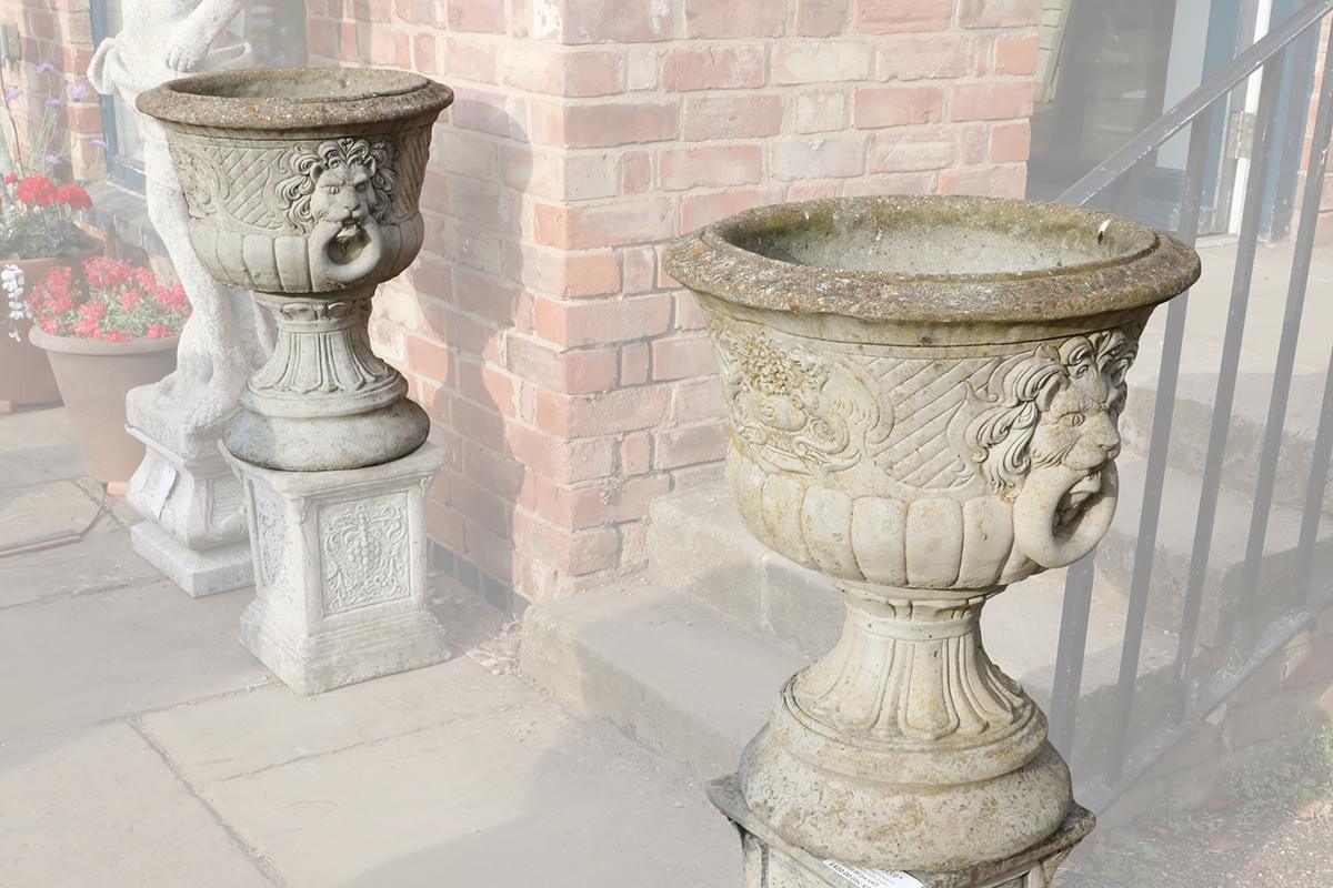 A pair of reclaimed decorative lions head urns in composite stone, showing a fine patina of discolouration and lichen patches, ready for planting