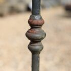 A detail of a wrought iron spear top railing section showing a rich patina of peeling paint and surface corrosion