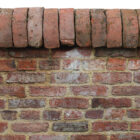 A run of antique red half round wall copings showing natural weathering and remnants of lime mortar