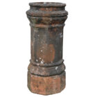A heavily weathered red octagonal chimney pot displaying a great patina of old soot staining and lichen.