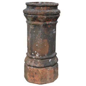 A heavily weathered red octagonal chimney pot displaying a great patina of old soot staining and lichen.