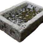 A small reclaimed stone sink with drain hole and patina of weathered edges, moss and worn rim