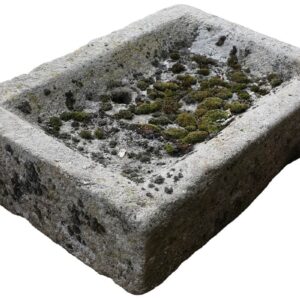 A small reclaimed stone sink with drain hole and patina of weathered edges, moss and worn rim