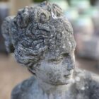 Detail of a reclaimed composite stone statue of Pandora with an authentic weathered patina of lichen and organic discolouration