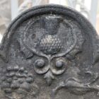 Detail of a heavily weathered, cast iron fire back with basket and dogs commemorating an historic battle in the North of England