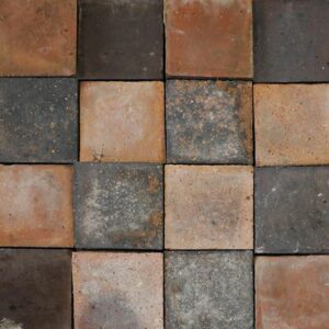 A batch of reclaimed red and blue quarry tiles laid in a classic chequerboard pattern, showing the pitted surfaces and discolouration commensurate with age