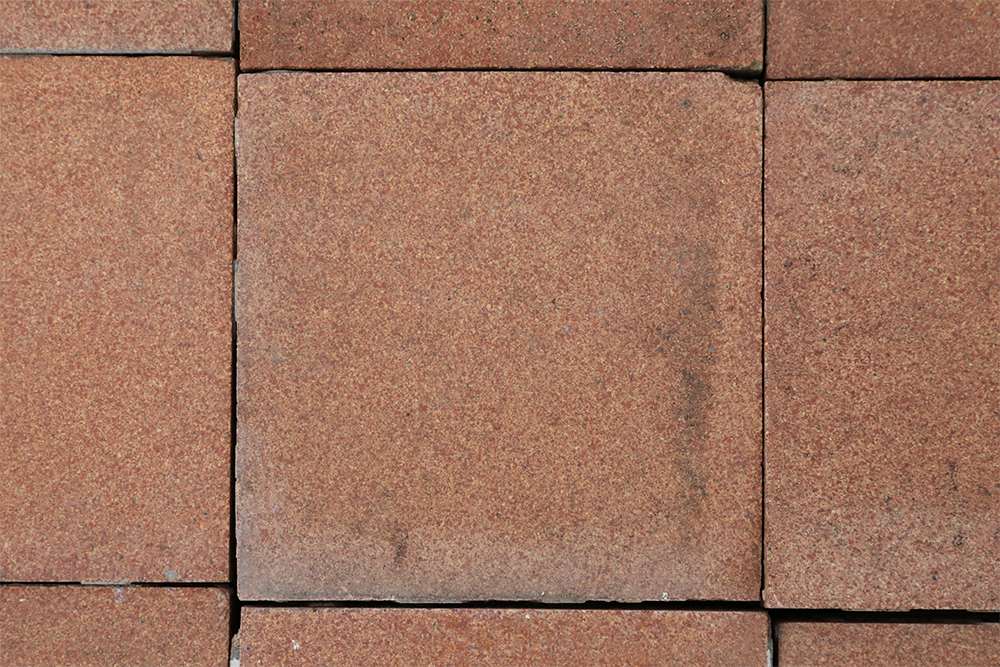 A close up of a tile from a wide spread of reclaimed 4 inch Heather Brown quarry tiles from the Dennis Ruabon Hafodex range, showing minor variation in colour and an aged patina of minimal edge wear and remnants of mortar.