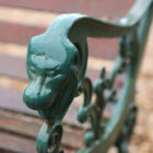 Detail of a lion head armrest on a weathered vintage wooden bench with cast iron ends