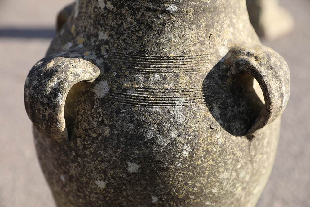Detail of a well weathered composite stone vase with four handles and a slim profile showing a lovely patina of discolouration and lichen.